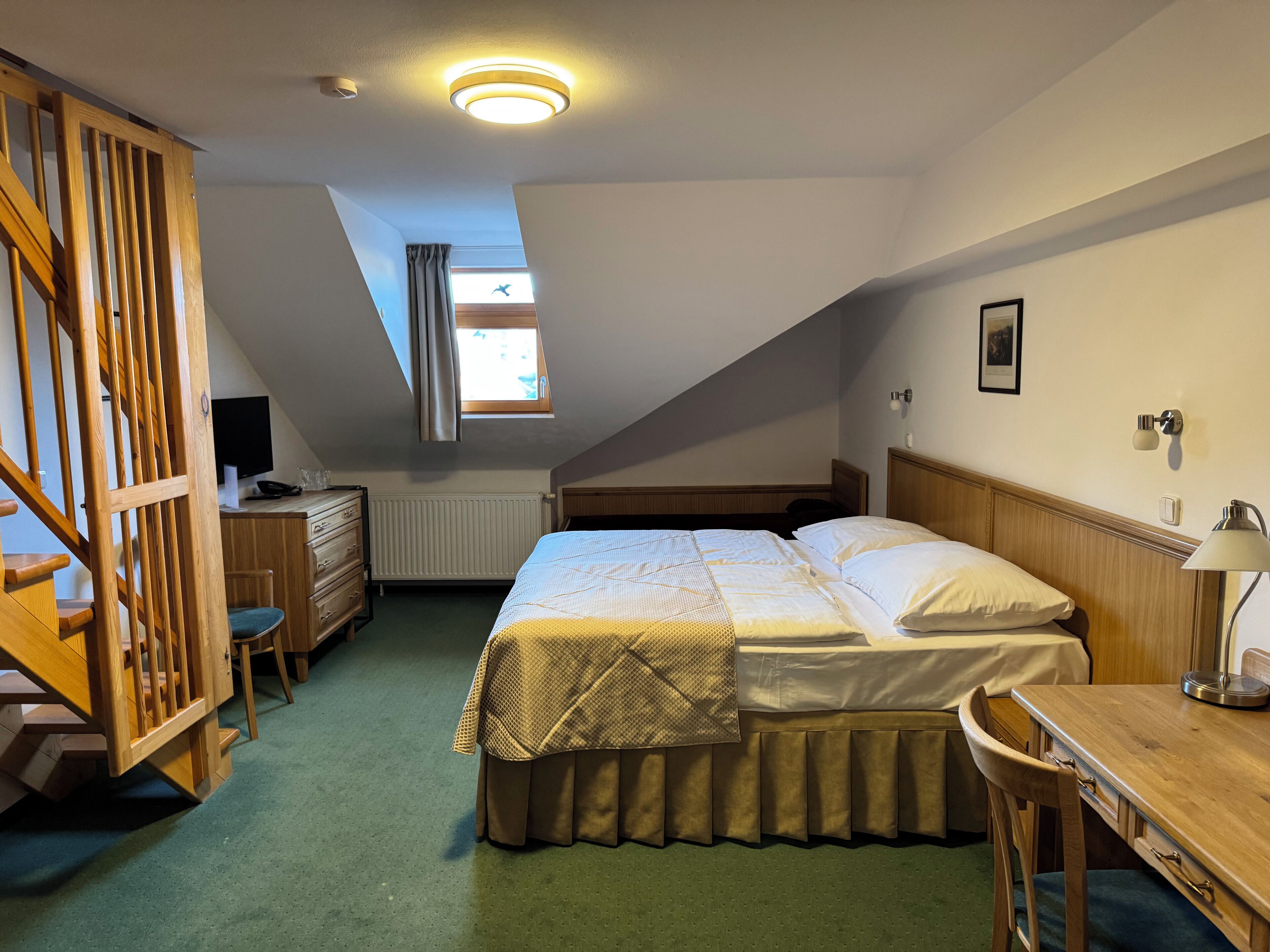 A bedroom with a bed, a desk, a chair, a dresser, a window with curtains, and a ceiling light.