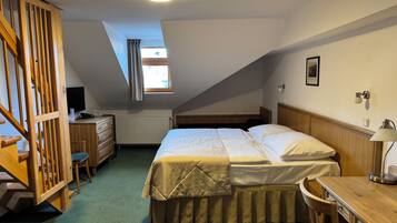 A bedroom with a bed, a desk, a chair, a dresser, a window with curtains, and a ceiling light.