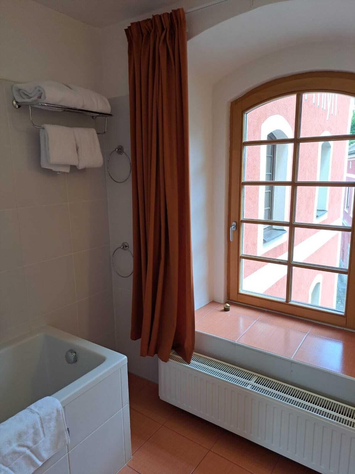 A bathroom with a bathtub, a window with a view of buildings, and a radiator.