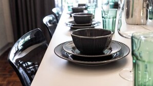 Ruokapöytä on katettu mustilla kulhoilla ja lautasilla, siinä on vihreä lasikannu ja hopeinen kannu.