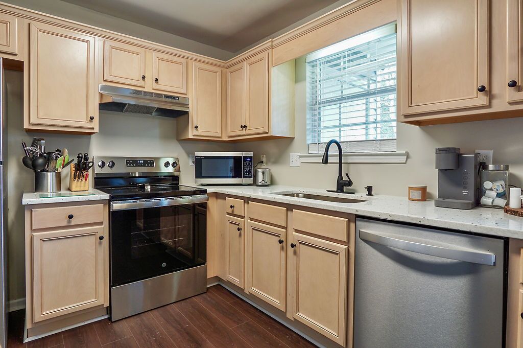 A kitchen with light wooden cabinets, a stainless steel stove, a microwave, a sink, and a dishwasher.