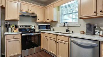 A kitchen with light wooden cabinets, a stainless steel stove, a microwave, a sink, and a dishwasher.