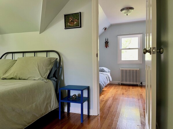 A bedroom with a bed, a small table, a radiator, and a window. - Village of Catskill Home (Catskill)