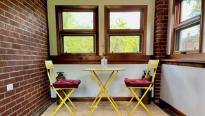 A small room with two windows, a brick wall, a yellow folding table, two yellow chairs, and a woven rug. - Village of Catskill Home (Catskill)