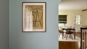 A framed abstract painting on a wall, a dining area with chairs and a table, and an arched doorway leading to another room. - Village of Catskill Home (Catskill)