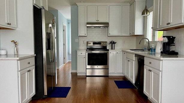 A modern kitchen with white cabinetry, stainless steel appliances, and a wooden floor. - Village of Catskill Home (Catskill)