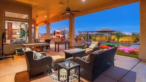 Ein Terrassenbereich im Freien mit Korbmöbeln, einem Deckenventilator und Blick auf einen angelegten Garten.