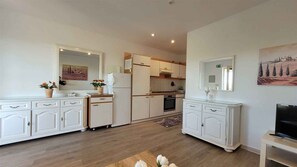 Eine moderne Küche mit weißen Schränken, einem Kühlschrank, einem Backofen und einer Mikrowelle. Es gibt einen Essbereich mit Tisch und Stühlen sowie einen Fernseher auf einem Schrank.
