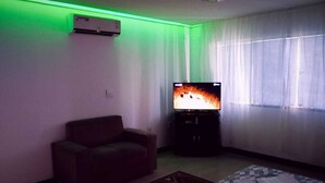 A living room with a sofa, a flat-screen TV, an air conditioner, and a patterned rug. - Accommodation close to the center, comfortable and safe, VIP Suite with living room. (Centro Feira de Santana)