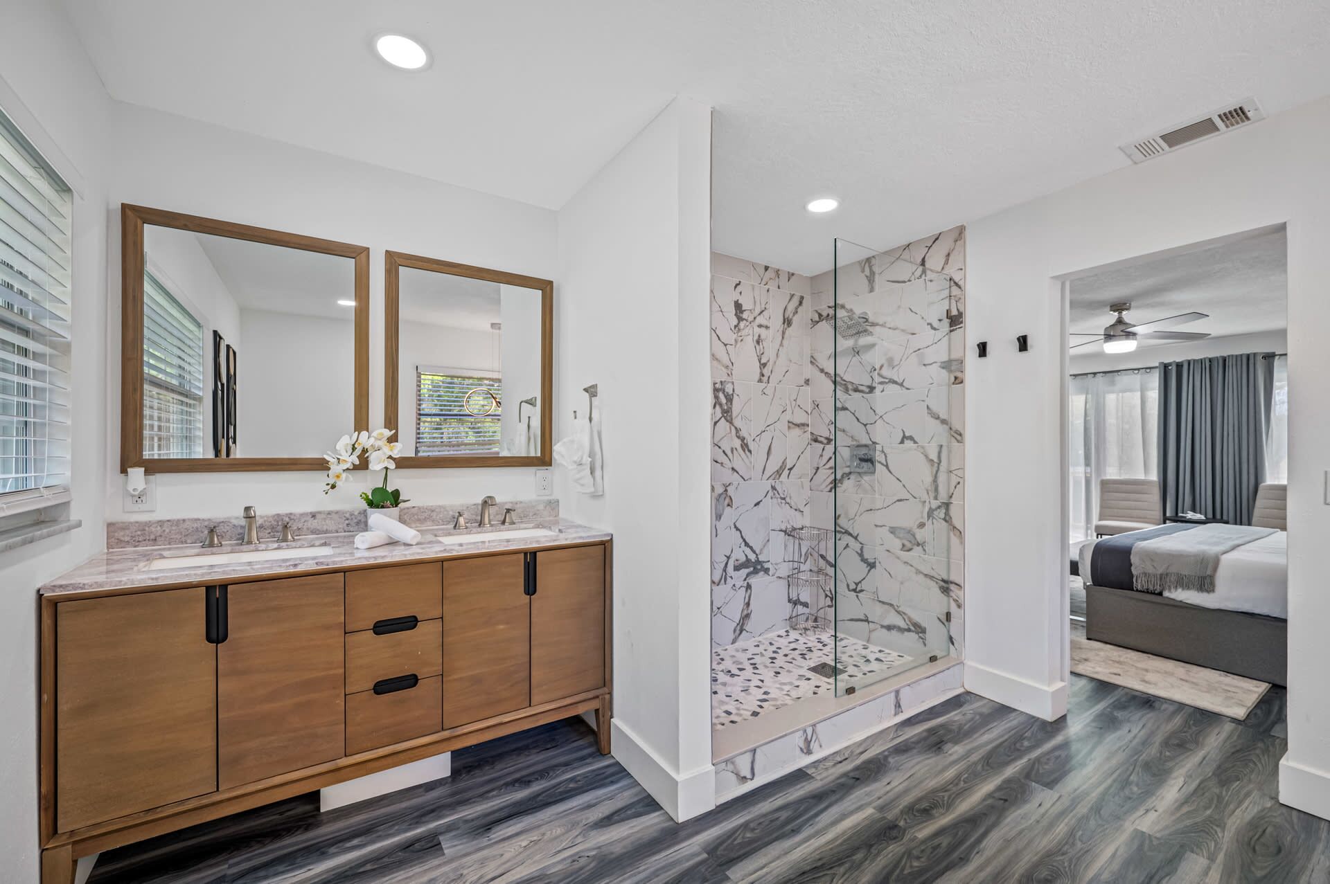 A modern bathroom with a marble shower wall, a wooden vanity with a sink, and a large mirror.