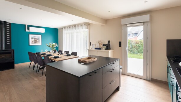 Eine moderne Küche mit Kochinsel, Essbereich mit Stühlen und Tisch, und ein großes Fenster mit Vorhängen.