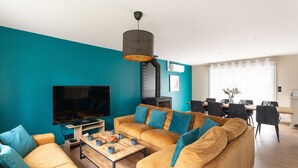Ein modernes Wohnzimmer mit einer Türkis-farbenen Akzentwand, einem großen Flachbildfernseher, einer Sofagarnitur und einem Essbereich mit Tisch und Stühlen.