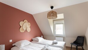 Ein Schlafzimmer mit zwei Betten, einem Sessel, einer Wanddekoration und einer Pendelleuchte.