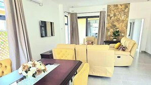 A modern living room with a dining area, featuring a dark wooden table, yellow upholstered chairs, and a beige sofa.