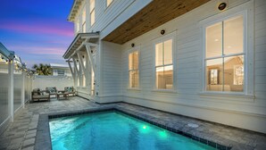 A swimming pool with a stone deck, white exterior walls, and large windows.