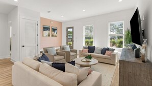 A modern living room with a beige sofa, armchairs, a coffee table, and a TV on a wooden stand.