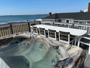 Un jacuzzi con vistas al mar, una terraza con mobiliario exterior y un edificio al fondo.