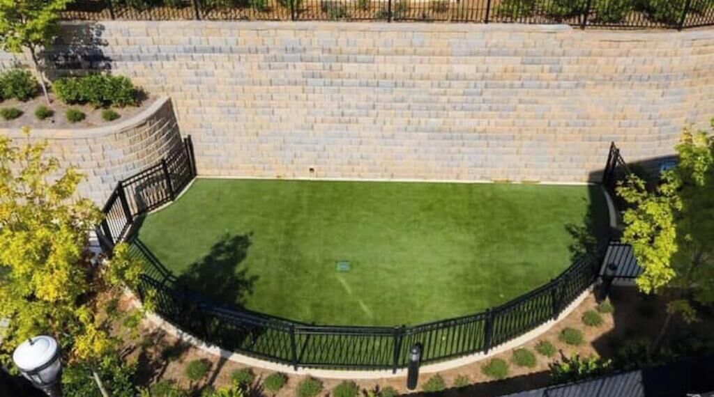 A circular lawn with a black metal fence, surrounded by a stone wall.