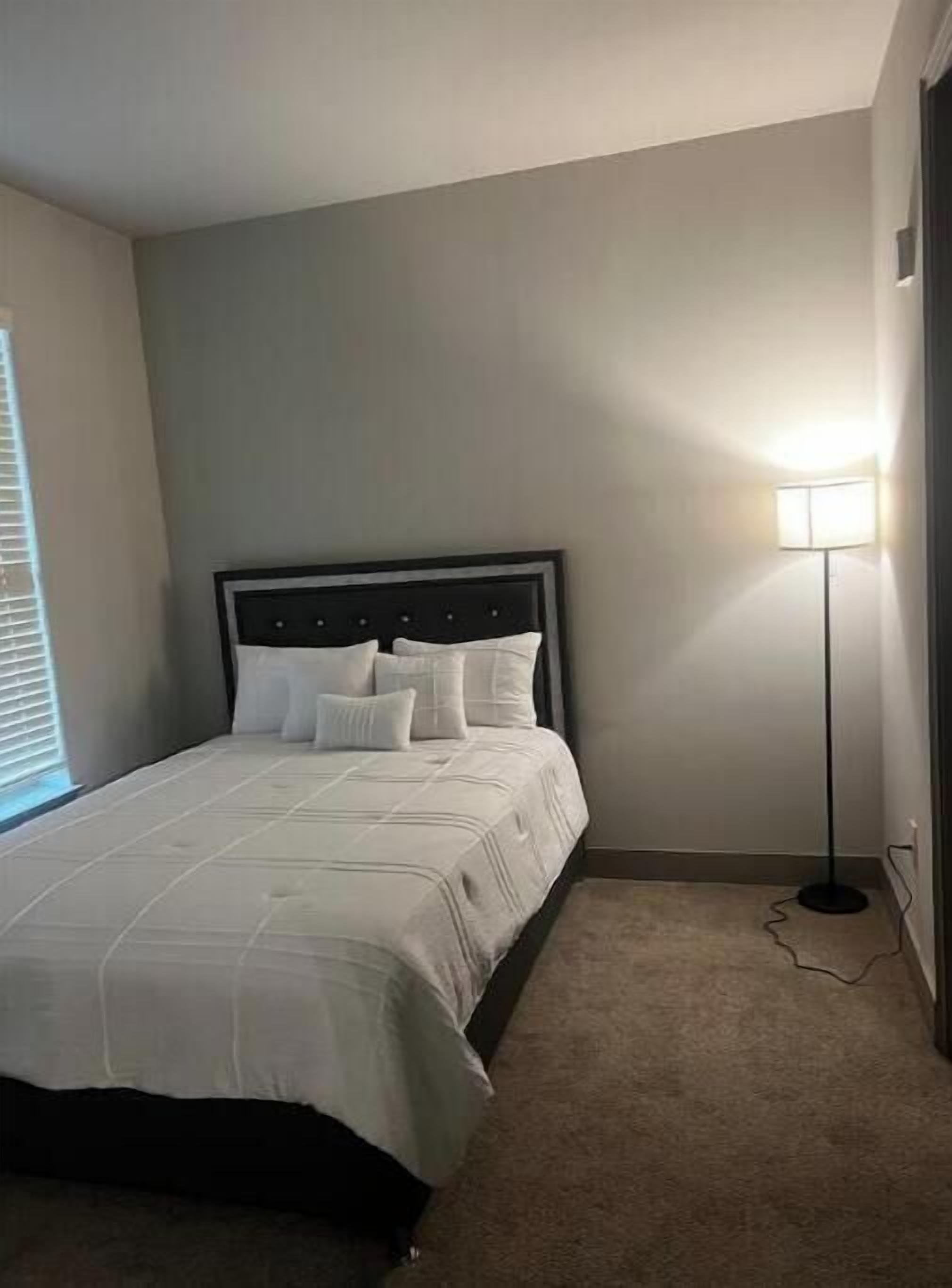 A bedroom with a bed, a floor lamp, and a window with blinds.