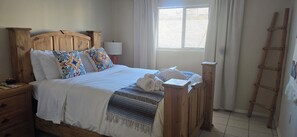 A wooden bed with white bedding, a bedside lamp, and a window with curtains.