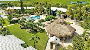 Un resort con piscina, edificaciones de techo de paja y exuberante vegetación.