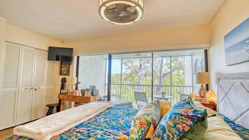 A bedroom with a large bed, a desk, and a view of the outdoors through a sliding glass door.
