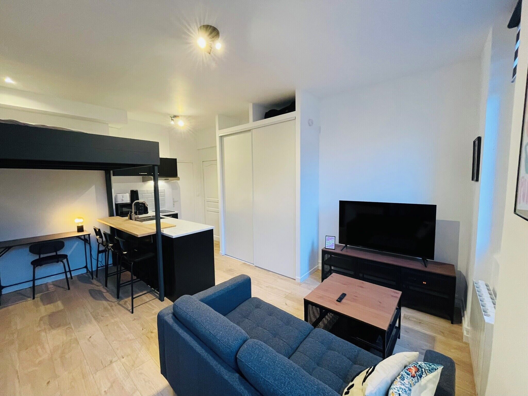 Ett kompakt bostadsutrymme med ett litet kök, en soffa, en TV och en matplats.