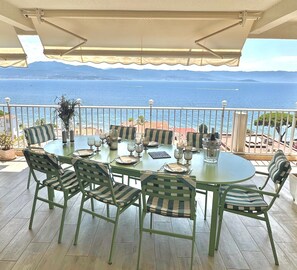 Een ronde tafel met stoelen en een gedekte tafel op een balkon met uitzicht op zee.