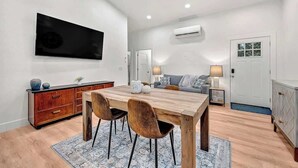 Ein modernes Wohnzimmer mit einem Holzesstisch, zwei Stühlen, einer Couch und einem an der Wand montierten Fernseher.