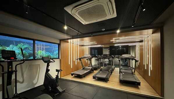 A gym with treadmills, an elliptical, and a stationary bike, featuring a large window with a view of greenery. - Beach Haus (João Pessoa)