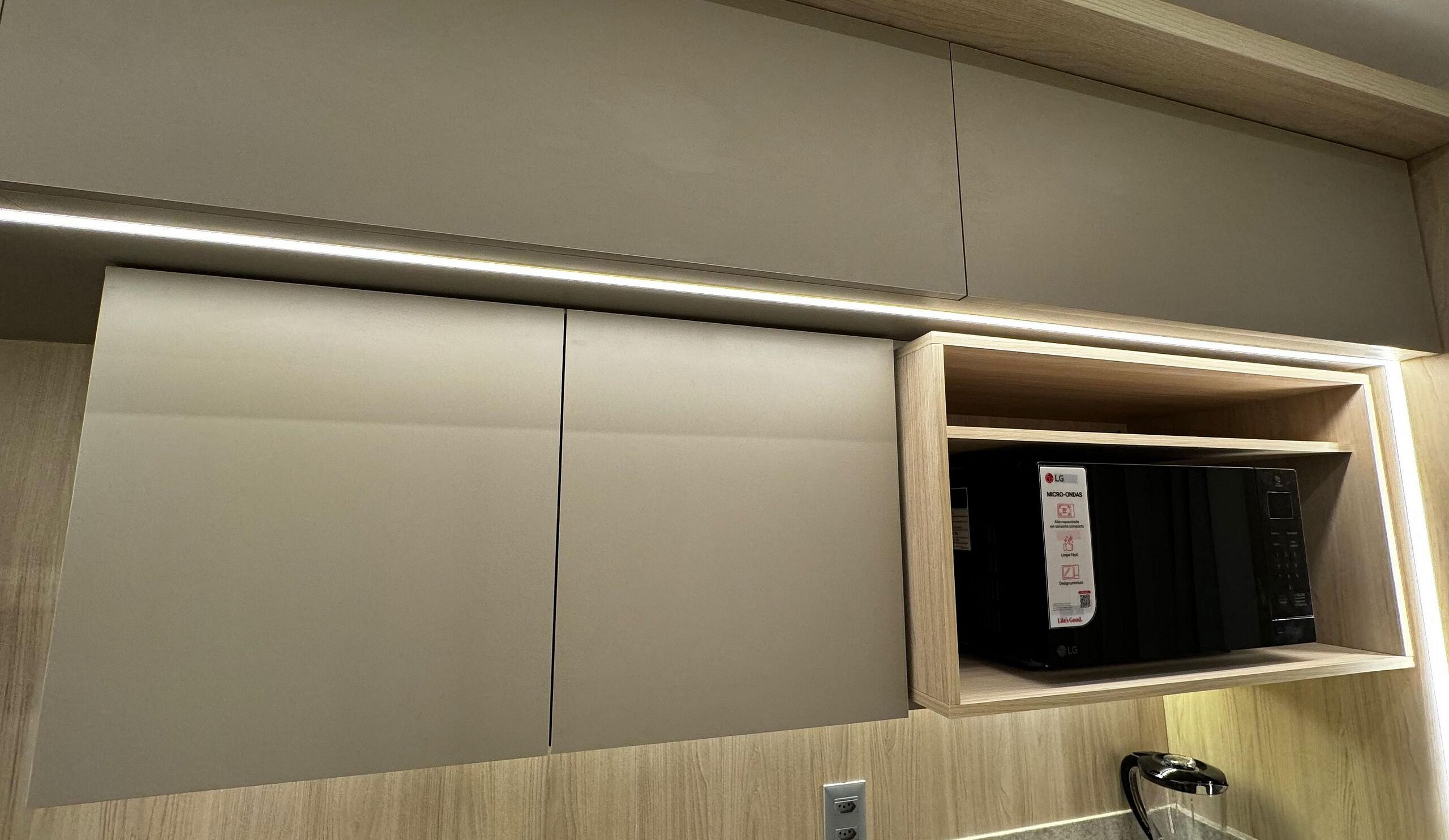 A kitchen with a microwave on a shelf, a cabinet with a sliding door, and a countertop with a coffee machine.