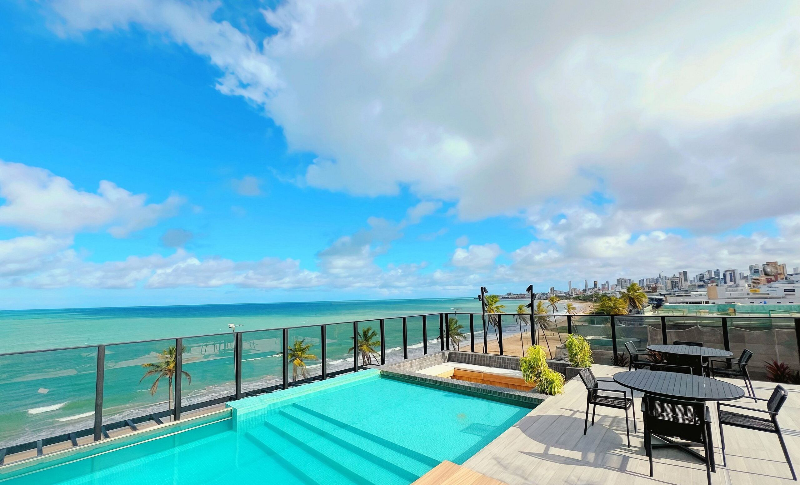 A rooftop pool with a view of the ocean and a city skyline.