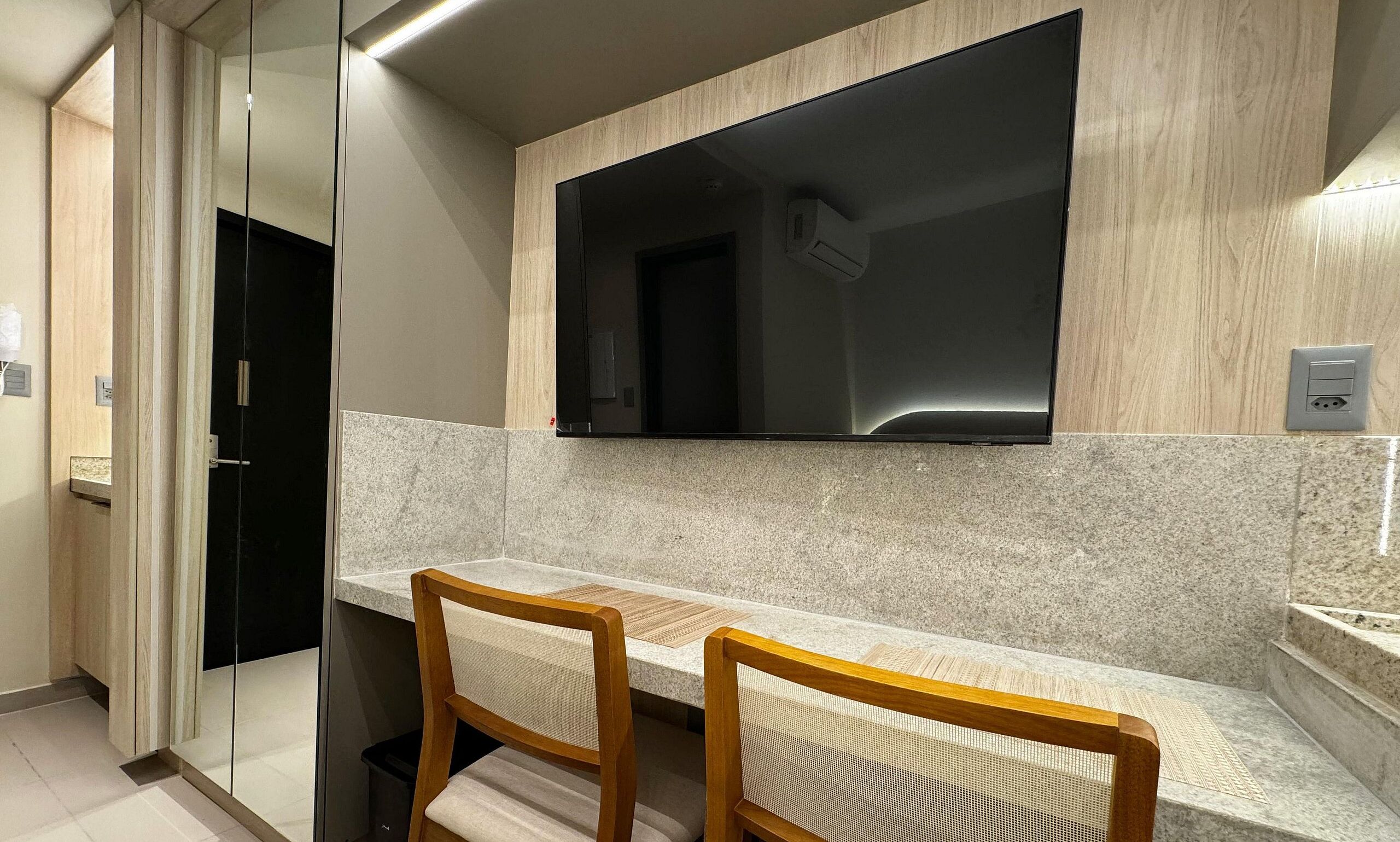 A modern kitchen with two wooden chairs, a built-in TV, and a granite countertop.