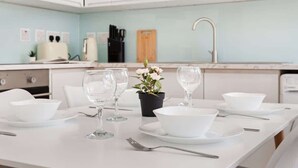 A clean, modern kitchen with white cabinets, a light blue backsplash, and a dining table set with white plates, bowls, and wine glasses.