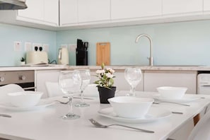 A clean, modern kitchen with white cabinets, a light blue backsplash, and a dining table set with white plates, bowls, and wine glasses.