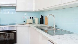A modern kitchen with white cabinets, a stainless steel sink, a built-in oven, and a light blue backsplash.