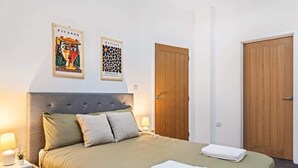 A bedroom with a bed, nightstands, a wooden door, and two framed artworks on the wall.