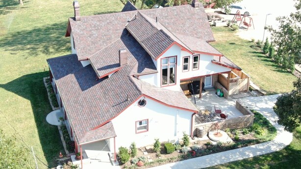 Une maison à deux étages avec un toit en pente, une terrasse couverte et une pelouse bien entretenue.