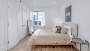 A modern bedroom with a bed, a bedside table, a chair, a window with curtains, and a framed picture on the wall. - Capitol Hill Suites- Unit 7 (Washington)