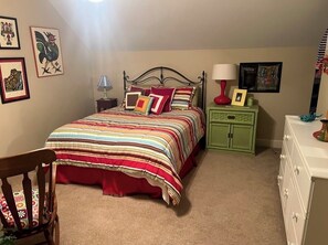 Cozy retreat with a neatly made bed, nightstand, and comfortable chair, surrounded by artwork and decorative pieces.