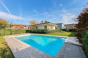 Une piscine rectangulaire avec une terrasse carrelée, entourée d’une pelouse bien entretenue et de haies.