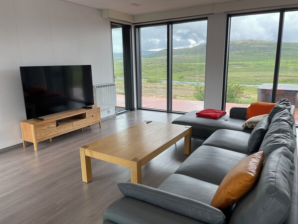 Una sala de estar moderna con un televisor de pantalla plana grande, una mesa de centro de madera y un sofá gris con cojines.