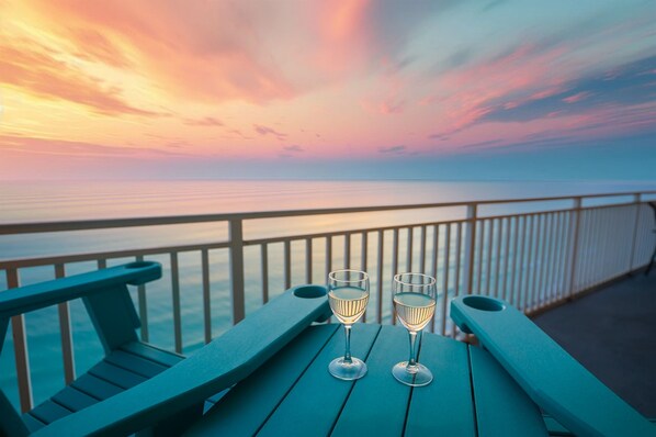 Une vue sur le coucher de soleil depuis un balcon, avec deux verres de vin posés sur une table en bois.