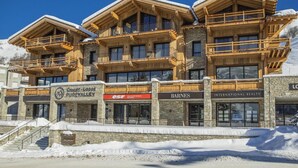 A multi-story lodge with wooden balconies and stone facade, featuring a restaurant, a bar, and a realty office. - 50m from shops, 2nd floor, sauna, terrace, balcony, fireplace or stove, parking, tv, 133m² (Les Menuires)