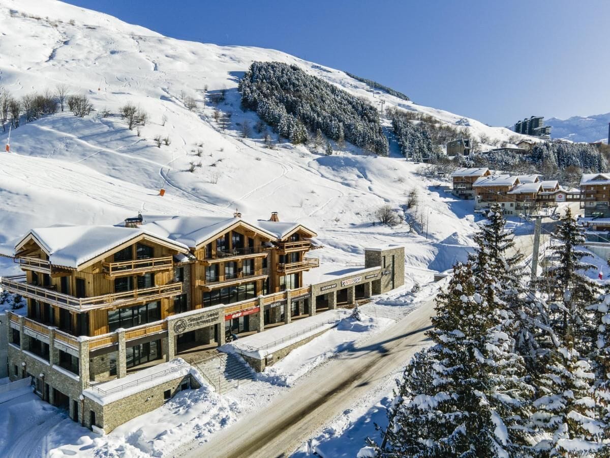 A multi-story wooden lodge with a ski lift in the background, surrounded by snow-covered slopes.