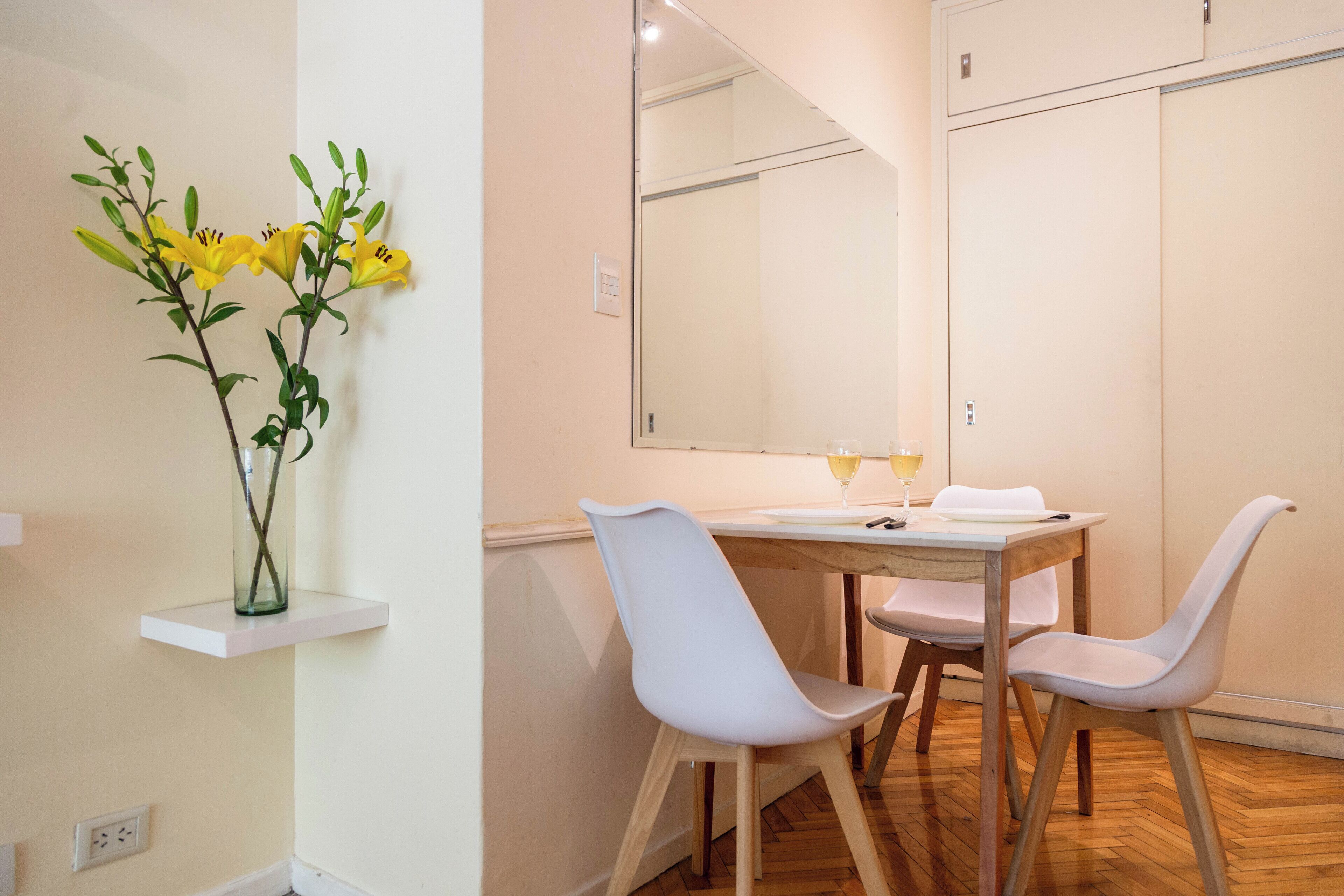 Et moderne spiseområde med et bord, stole og en vase med gule blomster på en hylde.