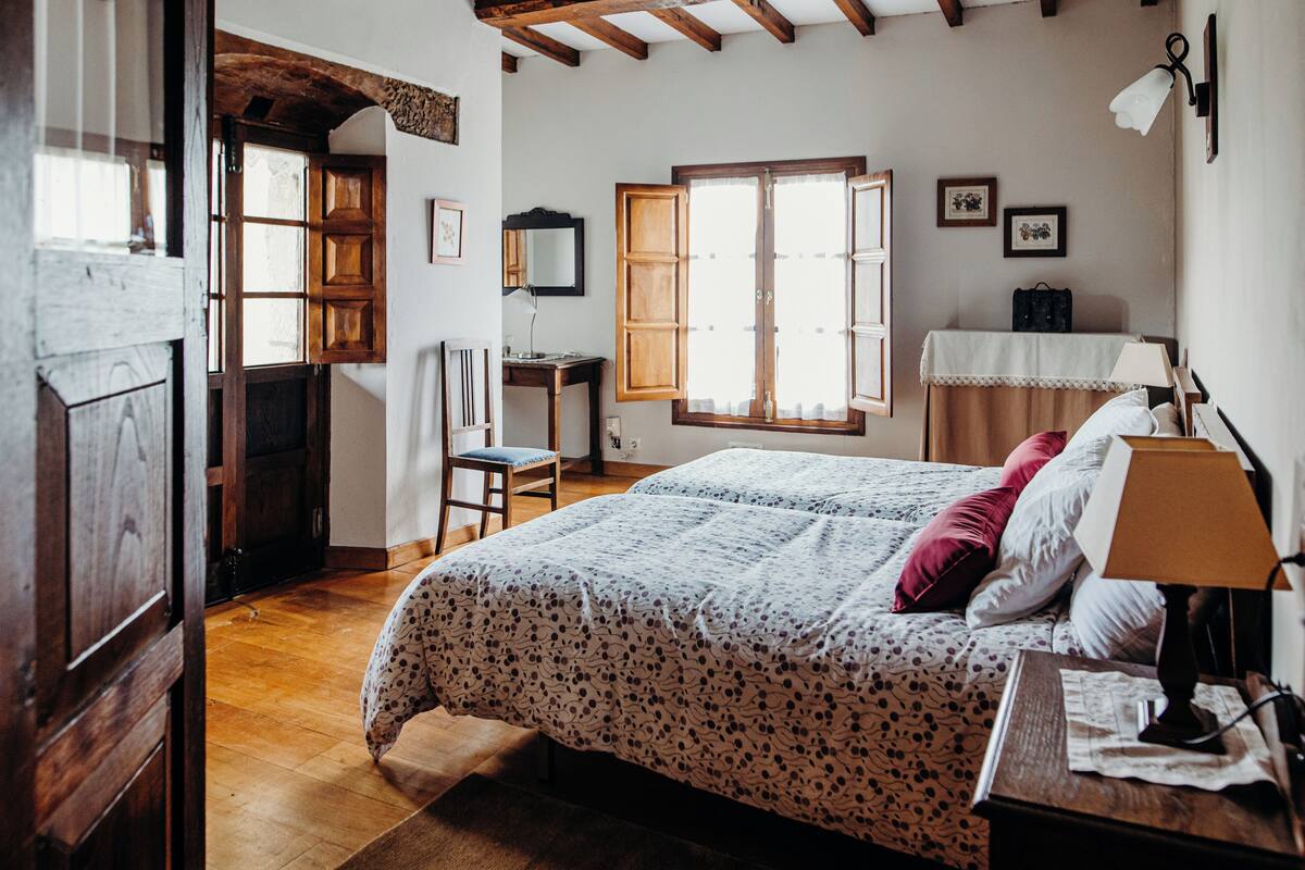 A bedroom with a bed, a desk, a chair, a window, and a lamp.
