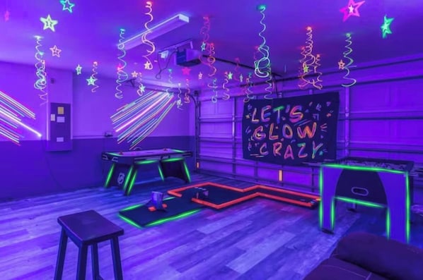 Een kamer met een neonbord waarop staat 'LET'S GLOW CRAZY', tafels met neonverlichting en een houten vloer.