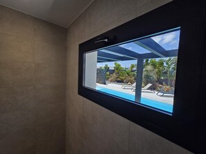 Une salle de bain moderne dotée d’une grande fenêtre donnant sur un espace piscine.