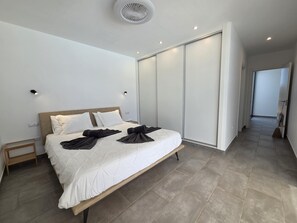Ein modernes Hotelzimmer mit einem großen Bett, einem begehbaren Kleiderschrank und einem Flur, der in ein weiteres Zimmer führt.
